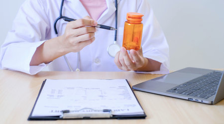 Female doctor holding a medicine bottle is checking the quality of medicine for any side effects the patient or not and recording patient information at the hospital. medical and health care concept.の写真素材