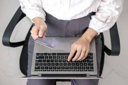 Asian woman shopping online using credit card and using laptop. Entering card number in laptop app to purchase and pay in online store.の写真素材