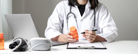Female doctor holding a medicine bottle is checking the quality of medicine for any side effects the patient or not and recording patient information at the hospital. medical and health care concept.の写真素材