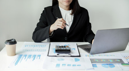 Asian businesswoman sit at their desks and calculate financial graphs showing results about their investments and plan successful business growth process.の写真素材