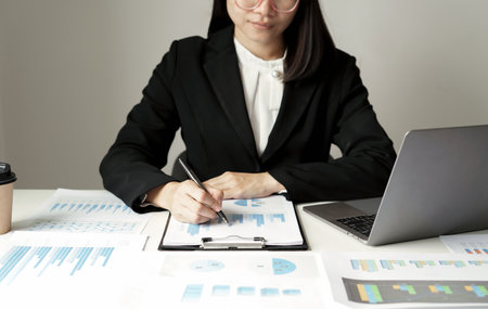 Asian businesswoman sit at their desks and calculate financial graphs showing results about their investments and plan successful business growth process.の写真素材