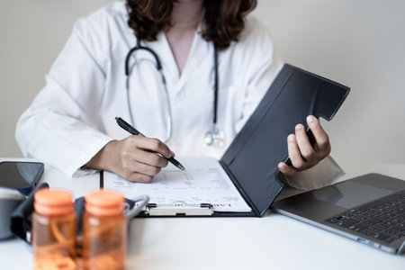 Female doctor holding a medicine bottle is checking the quality of medicine for any side effects the patient or not and recording patient information at the hospital. medical and health care concept.の写真素材