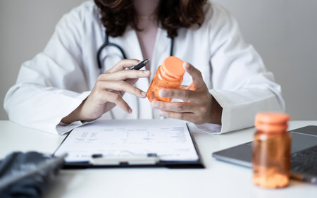 Female doctor holding a medicine bottle is checking the quality of medicine for any side effects the patient or not and recording patient information at the hospital. medical and health care concept.の写真素材