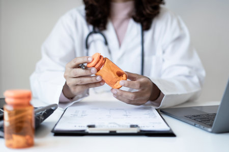 Female doctor holding a medicine bottle is checking the quality of medicine for any side effects the patient or not and recording patient information at the hospital. medical and health care concept.の写真素材