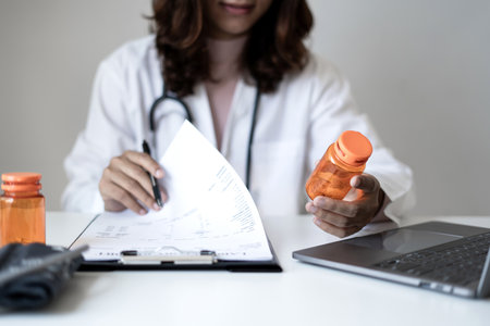 Female doctor holding a medicine bottle is checking the quality of medicine for any side effects the patient or not and recording patient information at the hospital. medical and health care concept.の写真素材