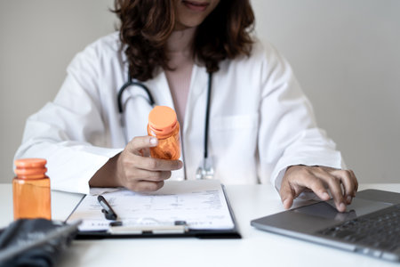 Female doctor holding a medicine bottle is checking the quality of medicine for any side effects the patient or not and recording patient information at the hospital. medical and health care concept.の写真素材