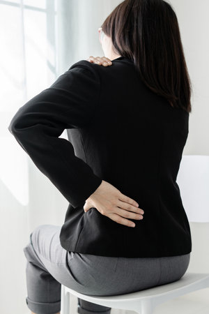 Woman having back and shoulder pain during work long time. stretching to relax while working hard at...