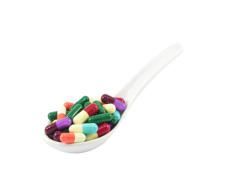 Colorful medicine capsules with spoon isolated on white background.