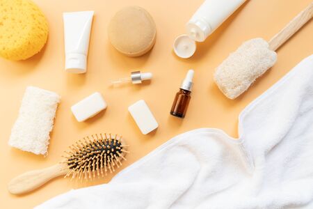Set of bath products on orange background. Top view of soap bar, shampoo, lotion, facial foam, essential oil, sponge, comb brush, loofah and towel. Aromatherapy and body care concept. Flat lay.の写真素材