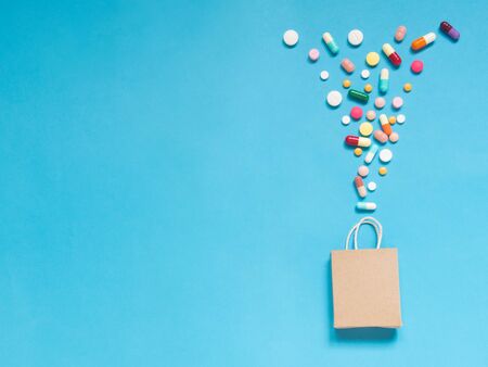 Shopping bag w/ assorted medicine pills on light blue background. Creative idea for dietary...