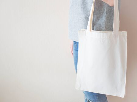 Blank white cotton tote bag with handle mock up design. Close up of woman holding eco or reusable shopping bag. No plastic bag and ecology concept. Copy space.の写真素材