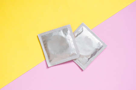 Condoms package on yellow pink background. A condom use to reduce the probability of pregnancy or sexually transmitted disease (STD). Safe sex and reproductive health concept.の写真素材