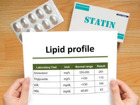 Physician checking blood laboratory results of lipid profile in high cholesterol patient and generic pack of statins tablets for treatment dyslipidemia on wood table. Health care and medical concept.の写真素材