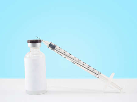 Blank label medical glass vial and plastic syringe for injection on white table with blue gradient background. Concept of vaccination, insulin and cosmetic injection. Copy space.の写真素材