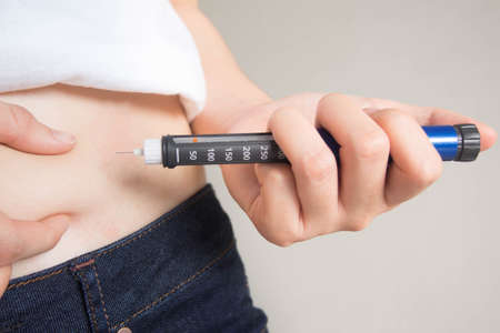 Close up of female diabetes patient making subcutaneous insulin injection into her abdomen with...