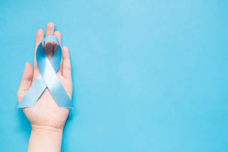 Men's health and Prostate cancer awareness campaign concept. Man hands holding light blue ribbon awareness on sky blue background. Symbol for support men who living w/ cancer. Copy space.の写真素材