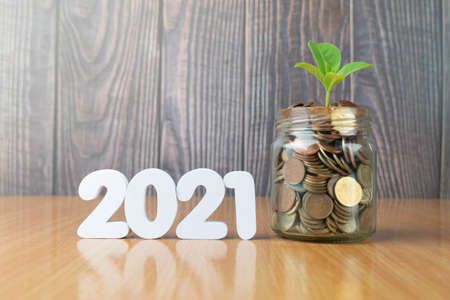 New year saving money and financial planning concept. Plants growing on glass of coins or piggy bank with 2021 number on wooden table. Idea for business growth and investment.の写真素材