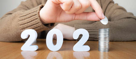 2021 New year saving money and financial planning concept. Female hands putting coins on stack with number 2021. Creative idea for business growth, tax payment, investment and banking.の写真素材