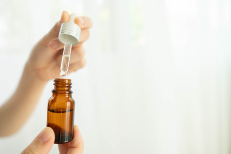 Skin care routine- Woman hands holding cosmetic brown glass bottle with dropper at home. Products of serum or essential oil. Aromatherapy, spa and beauty concept. Copy space.の写真素材
