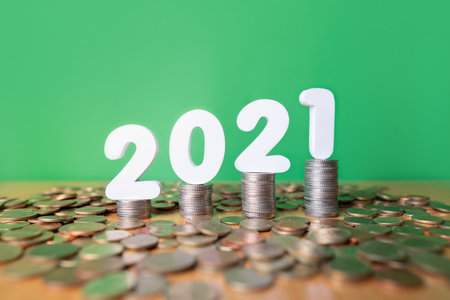 2021 New year saving money and financial planning concept. Stack of coins with number 2021 on wood table over green background. Creative idea for business growth, investment, profit and banking.の写真素材