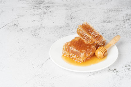 Fresh honeycombs with wooden honey dipper on white plate. Healthy food concept. Copy space.の写真素材