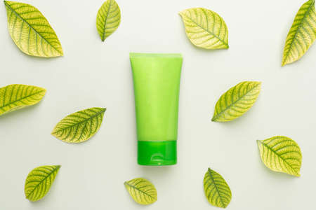 Natural herbal skincare products mock up. Top view of green squeeze bottle plastic tube with fresh leaves on green background. Packaging of lotion, cream, facial foam, gel, soap or shampoo.の写真素材