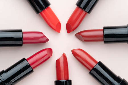 Red lipsticks of different shades arranged in a circle on beige background. Makeup and cosmetics concept. Close up. Flat layout.