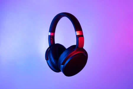 Black wireless bluetooth headphones on neon light background. Music concept.の写真素材