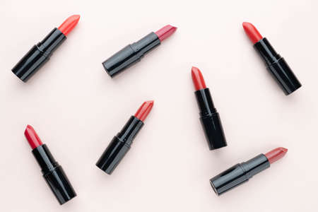 Red lipsticks of different shades  in black tube package on beige background. Makeup and cosmetics concept. Flat layout.の写真素材