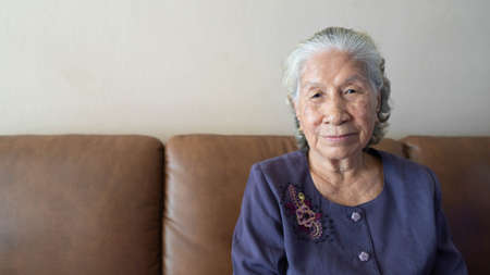 Happy senior asian woman smiling while sitting on a couch at home. Healthy living for the elderly concept.の写真素材