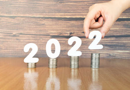 2022 New year saving money and financial planning concept. Hand putting numbers 2022 on stack of coins on wooden table. Creative idea for business growth, tax payment, investment and banking.の写真素材