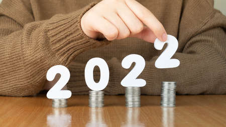 2022 New year saving money and financial planning concept. Female hands putting white number 2022 on stack of coins. Creative idea for business growth, tax payment, investment and banking.の素材 [FY310176492120]