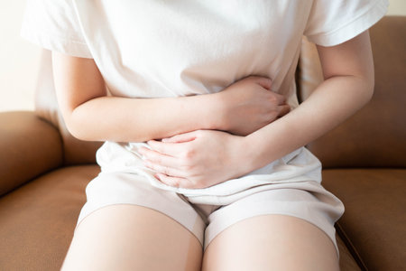 Young female suffering form stomach ache while sitting on couch at home. Causes of abdominal pain include menstruation pain, gastritis, stomach ulcer, food poisoning, diarrhea or IBS.の写真素材