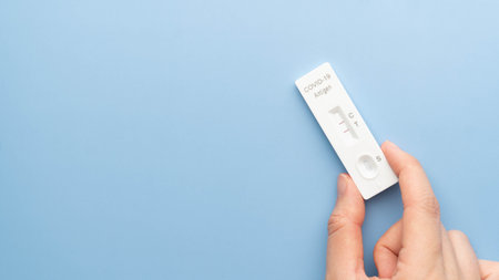 Woman hands holding SARS CoV-2 Rapid Antigen Test kit (ATK) with positive result during swab  testing on blue background.の写真素材