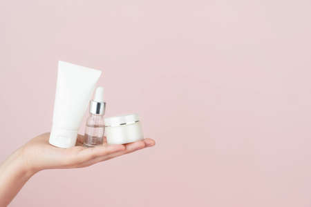 Skincare routineâ for healthy skin. Woman hand holding facial foam tube, serum bottle, moisturizingâ cream on pink background. Beautyâ and cosmetic concept.の写真素材