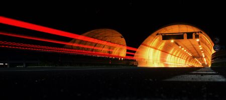 Street at night with red trails of cars in front of a tunnelの写真素材