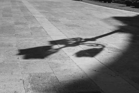 Black and white elongated shadow of a lamppost on a white cobbled square. Black and white. Shadow and light,の写真素材