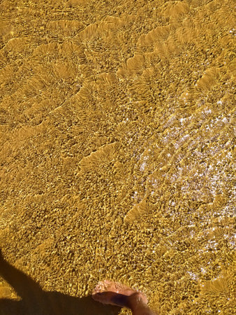 Bright ripples on the surface of the water. Golden sand beneath the brilliant ripples on the surface of the water. Shallow water beach surface, blurred abstract background.の写真素材