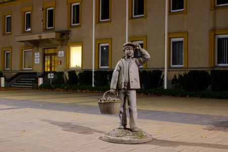 Varena, Lithuania - November 2 2022: Stone statue of a boy with a basket full of mushrooms. In the night city.のeditorial素材