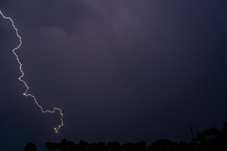 Rainy sky on a summer night with a flash of lightning on the left side of the sky, with the roofs of buildings rural.の写真素材