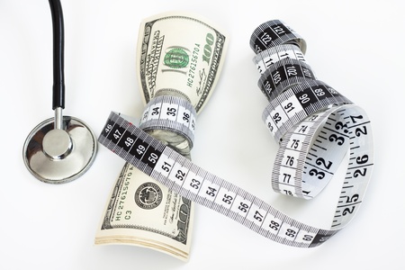 a bunch of dollar bills tighten by a measuring tape  and a stethoscope on white backgroundの写真素材