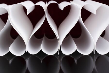 white paper hearts in a raw with reflection on black surfaceの写真素材
