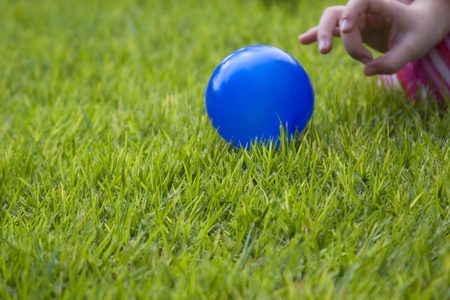 child playing with a blue ball on green grassの写真素材