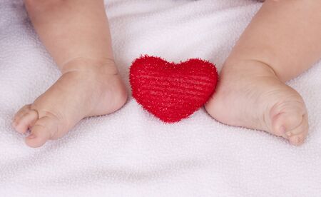 small baby feet with red heart between on white backgroundの写真素材
