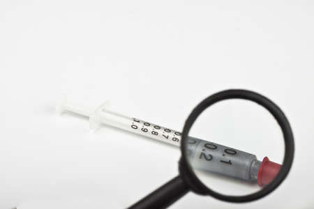 syringe with a magnifying glass on white backgroundの写真素材