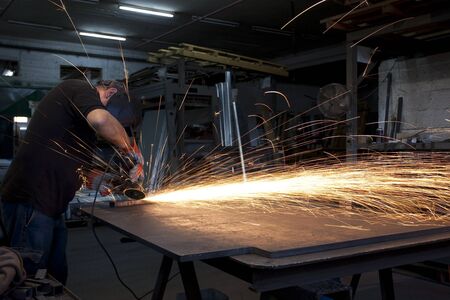proffesional heavy industry worker with all the safety equipment grinding metal with flying sparks...
