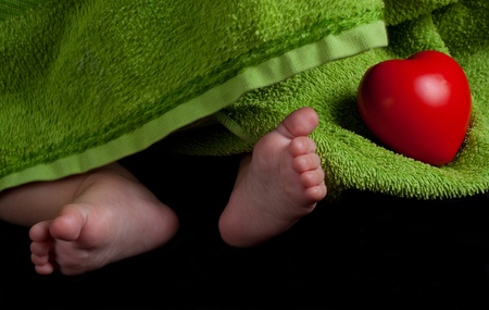 Baby feet and a red heart covered with green towel on balck backgroundの写真素材