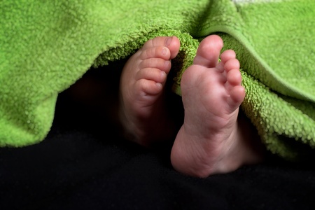 baby feet with green towel on black background