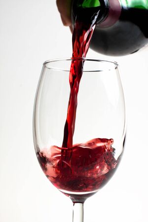 red wine puring from bottle to glass close-up on white backgroundの写真素材
