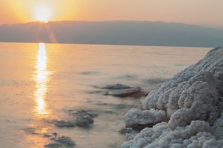 Sunrise in the dead sea with salt formations on the shoreの写真素材